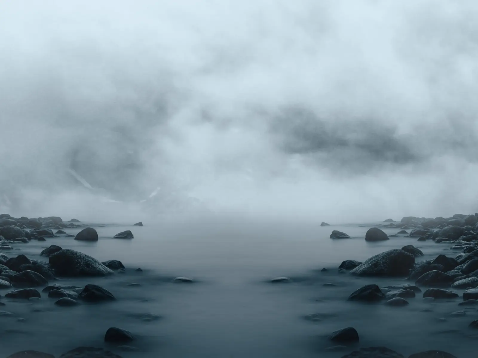 A black channel between rocky shores disappearing into dense gray fog